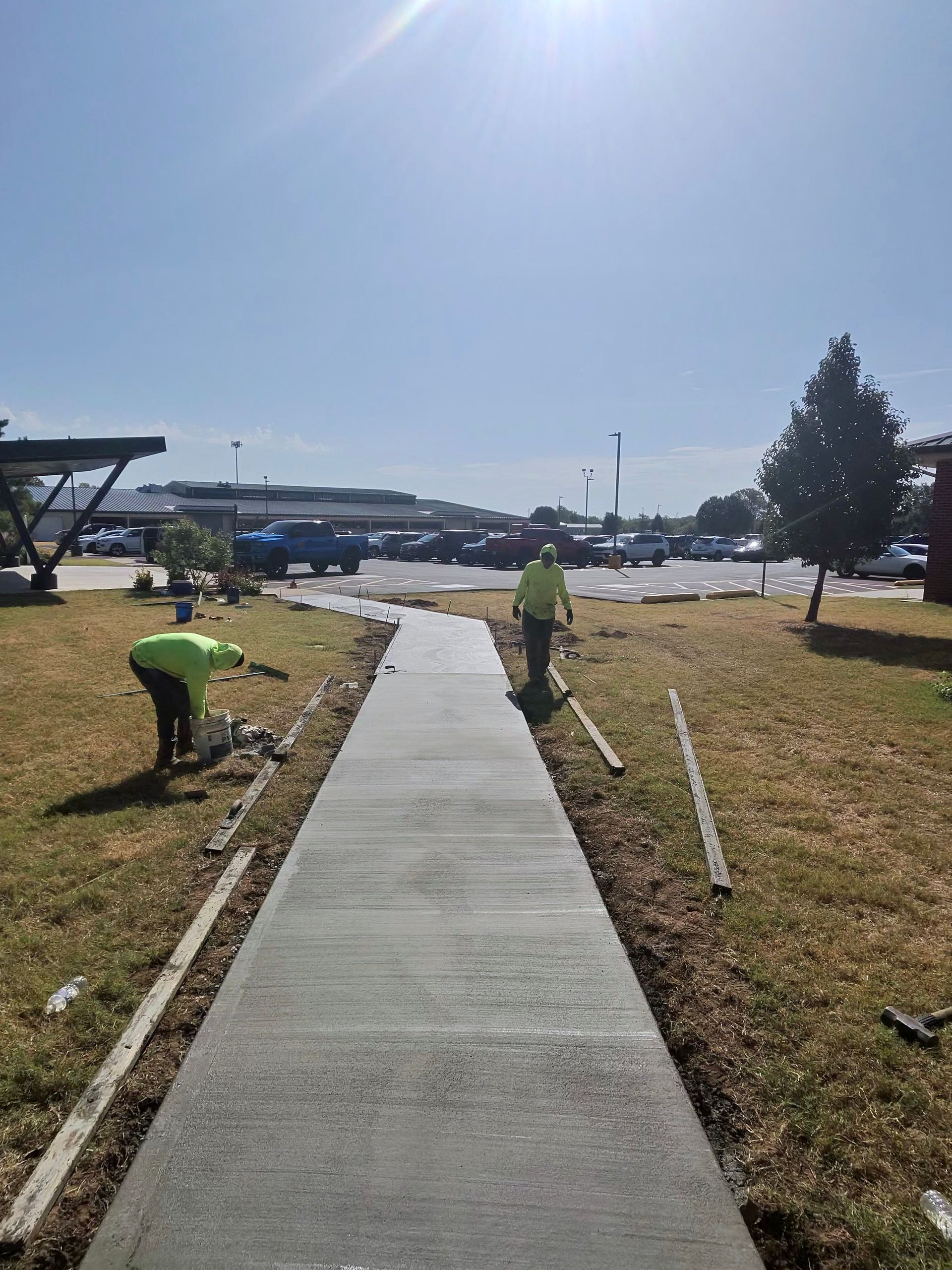 Concrete sidewalk under construction with workers in green shirts on a sunny day