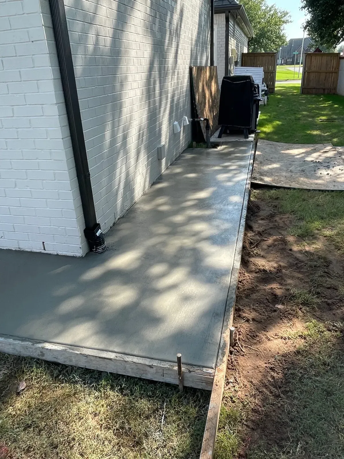 Newly poured concrete walkway next to a white brick building, surrounded by grass.