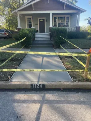 New concrete sidewalk with yellow caution tape in front of a house; address 1124.