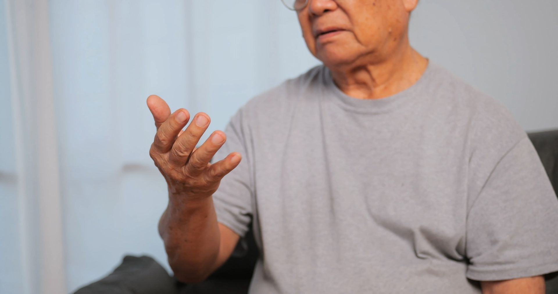 Ein älterer Mann sitzt mit ausgestreckten Händen auf einem Sofa Parkinson Ergotherapie