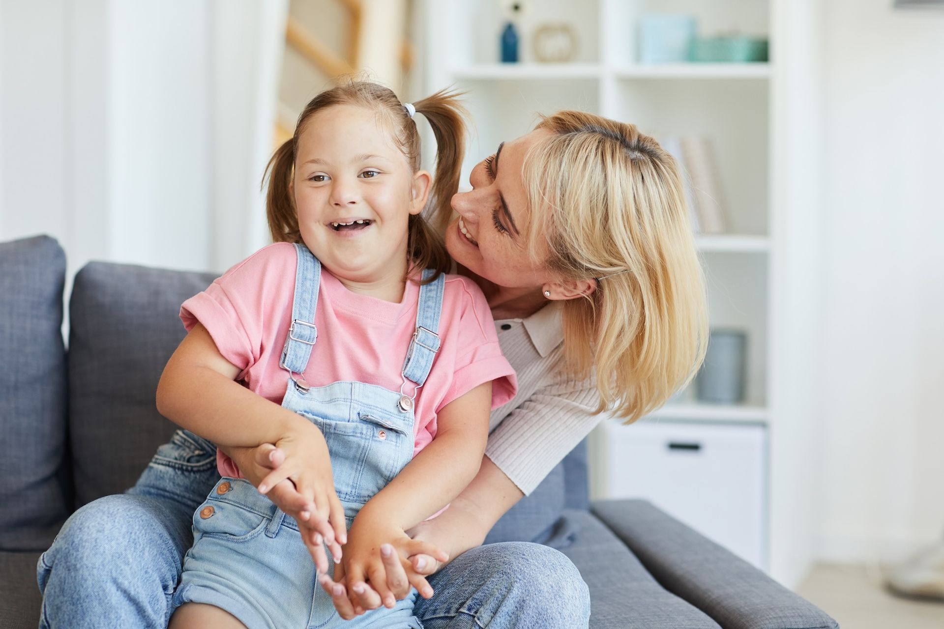 Eine Frau sitzt auf einem Sofa und hält ein kleines behindertes Mädchen im Arm. Körperliche Behinderung mit Ergotherapie behandeln