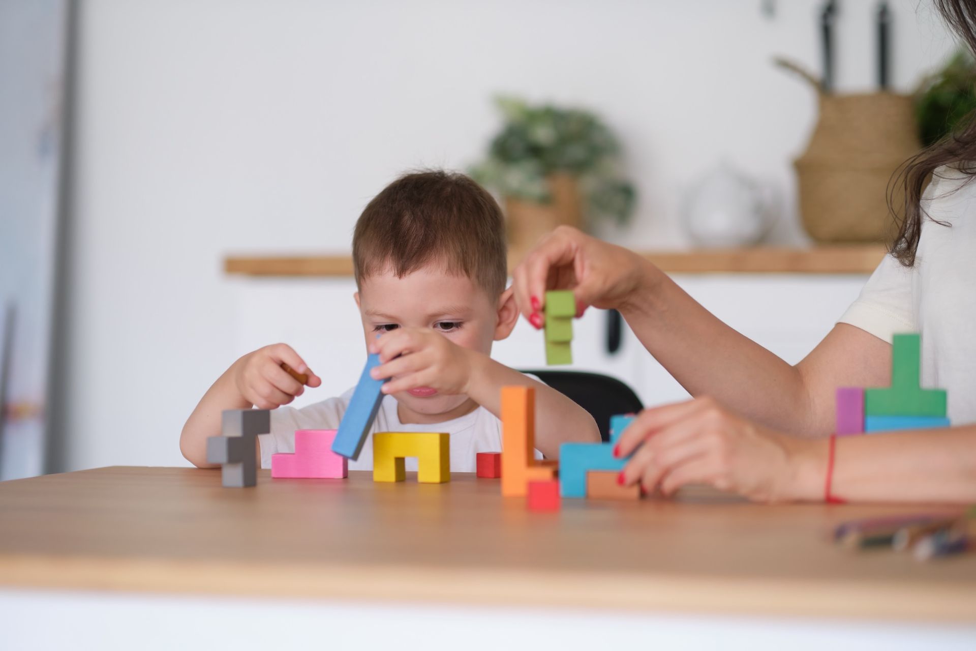Eine Frau und ein Kind spielen an einem Tisch mit Holzklötzen.