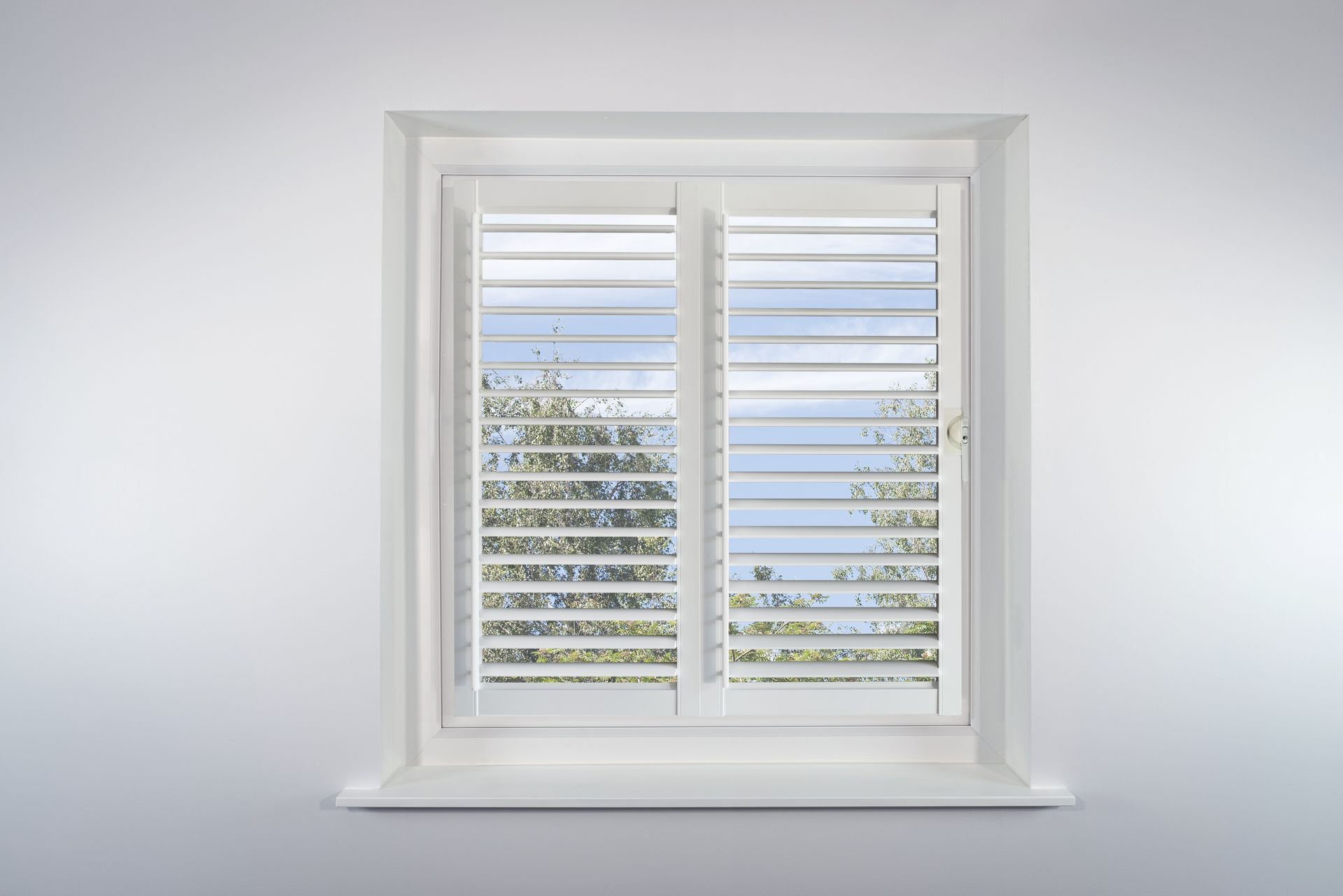 A white window with shutters on it is against a white wall.