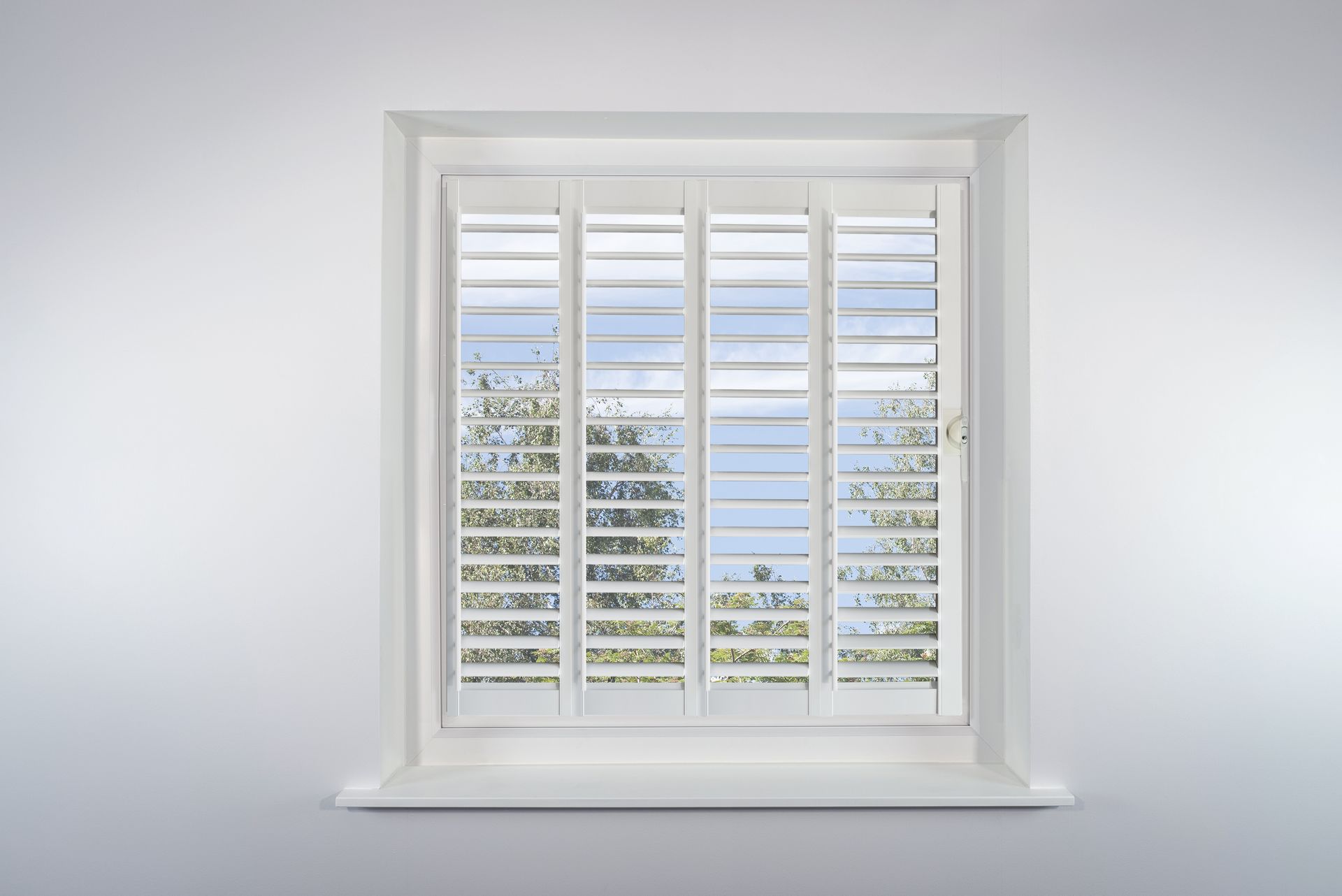 A window with white shutters on it is against a white wall.