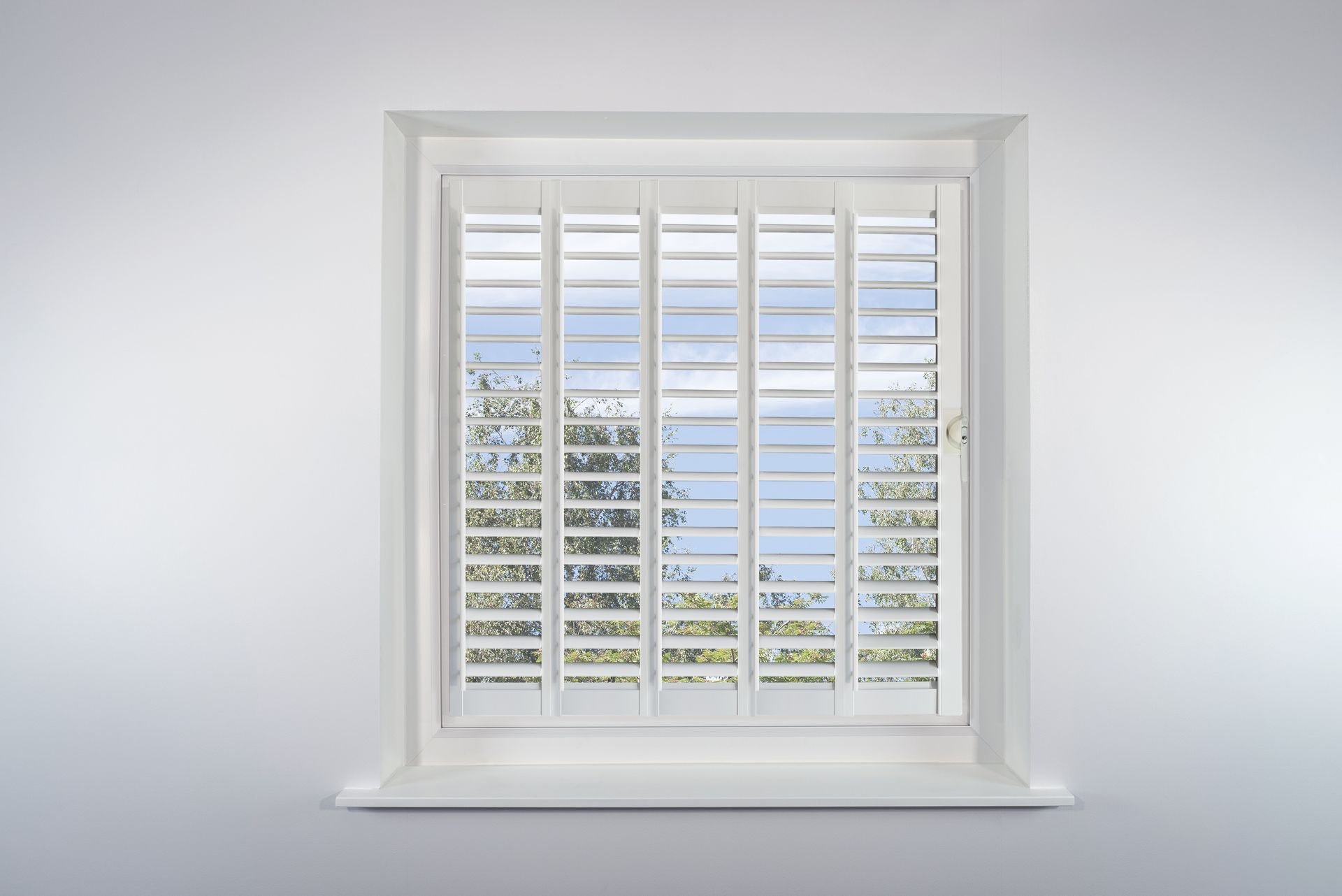 A window with white shutters on it is against a white wall.