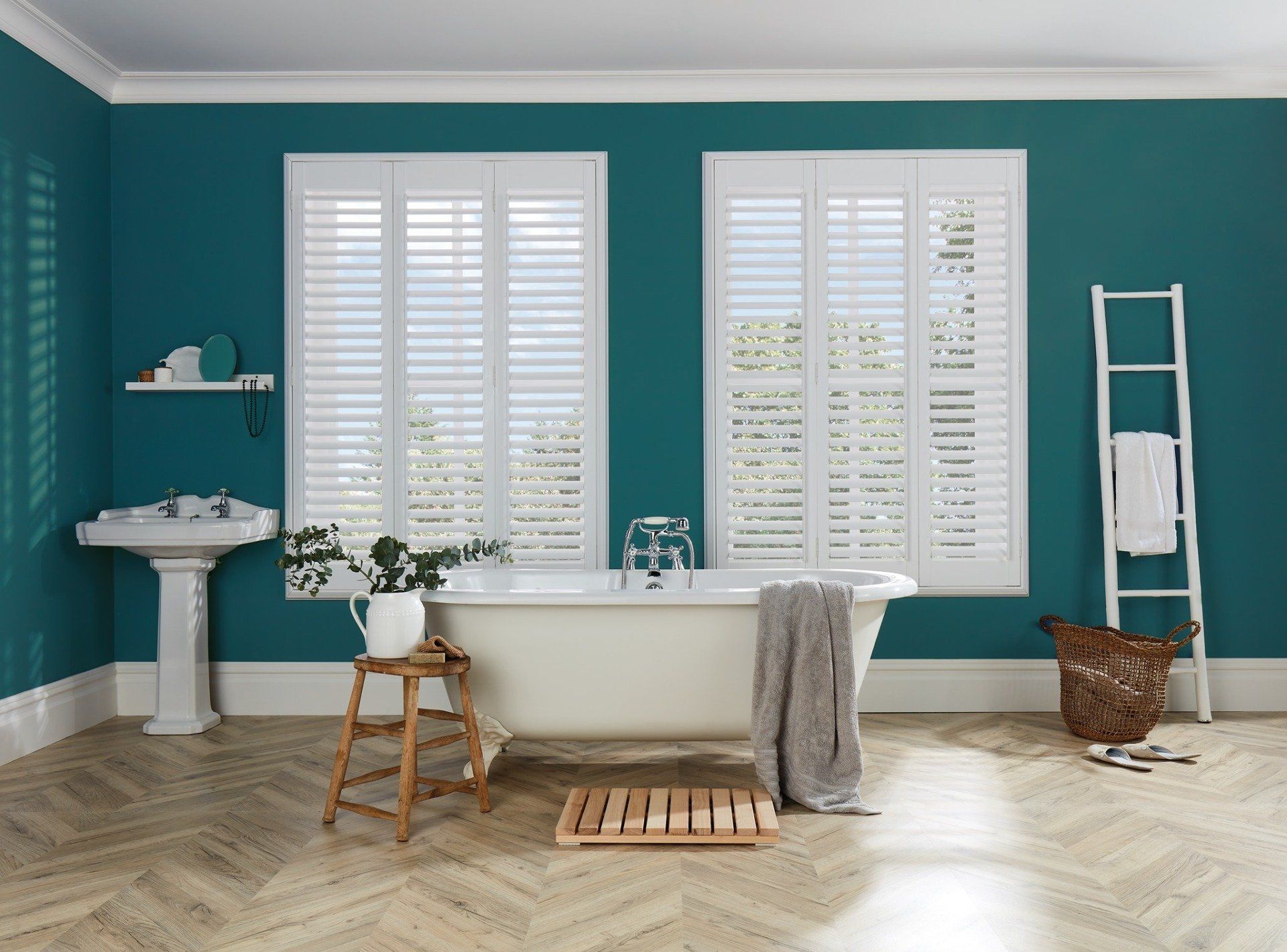 A bathroom with a bathtub , sink , and shutters on the windows.