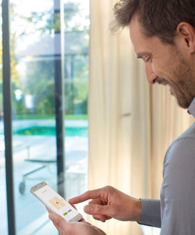 A man is using a smart phone in front of a window.