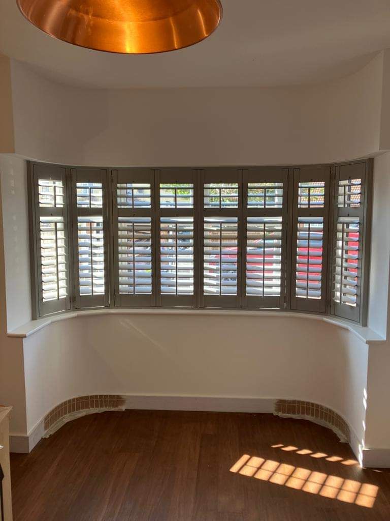 A room with a large bay window with shutters on it.
