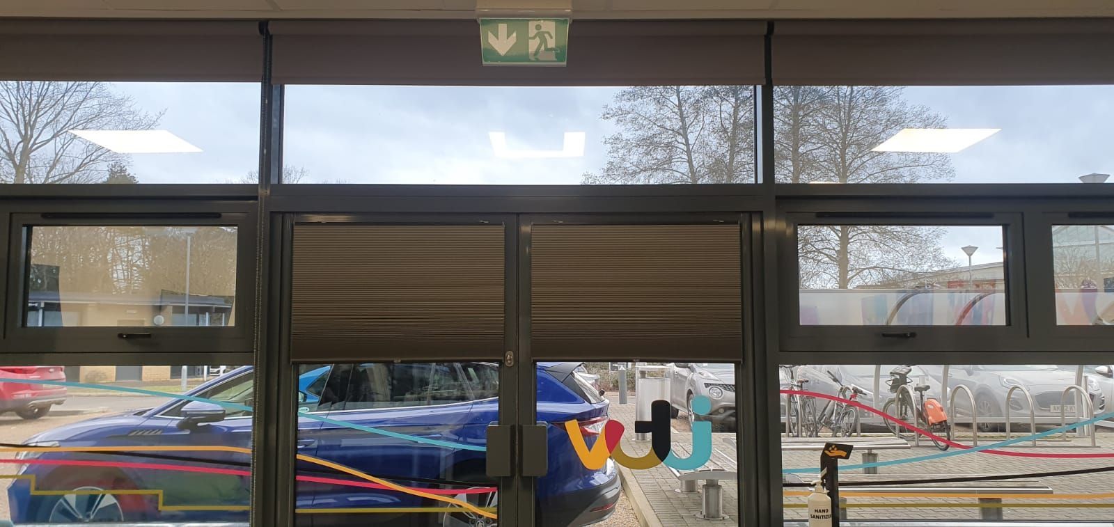 A car is parked in front of a building with a green exit sign above the door.