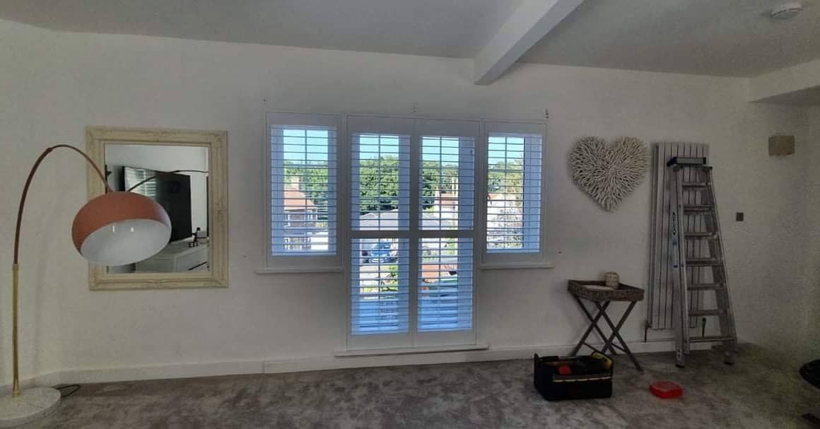 A living room with a lamp , mirror , and shutters on the windows.