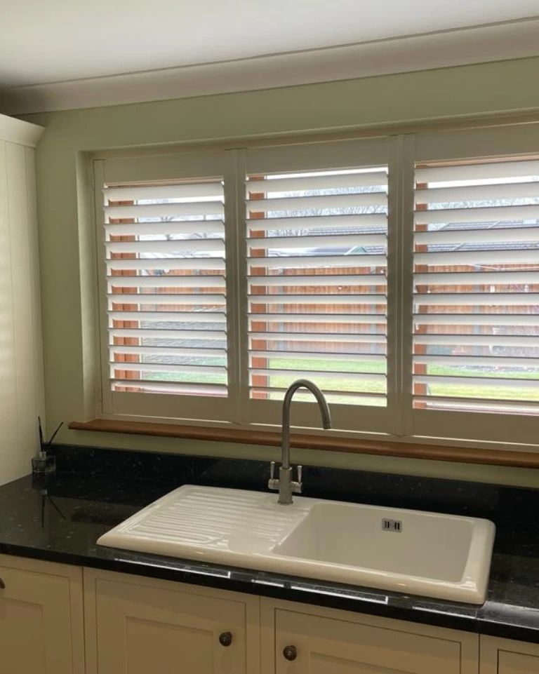 A kitchen with a sink and shutters on the windows