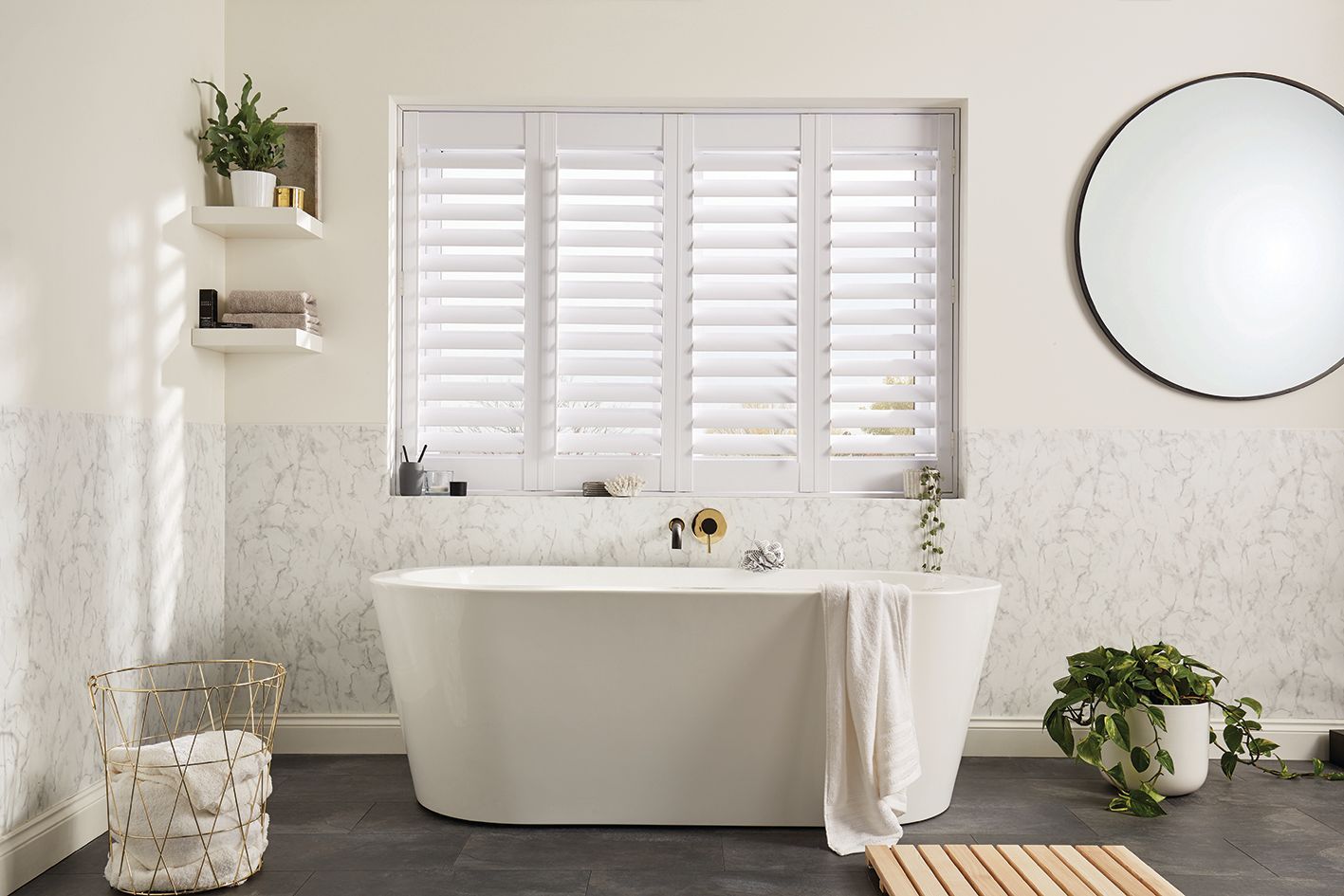 A bathroom with a bathtub , mirror , shutters and a window.