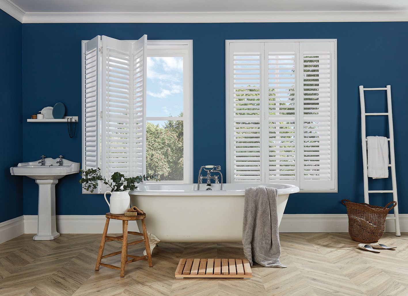 A bathroom with blue walls and white shutters on the windows.