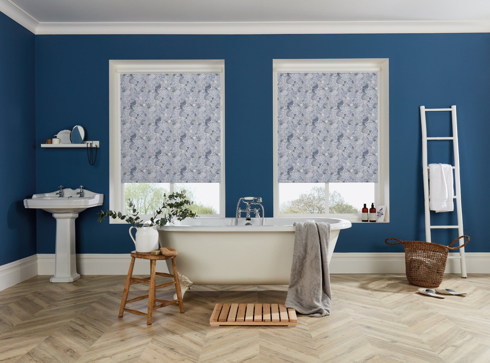 A bathroom with blue walls , a bathtub , a sink and two windows.