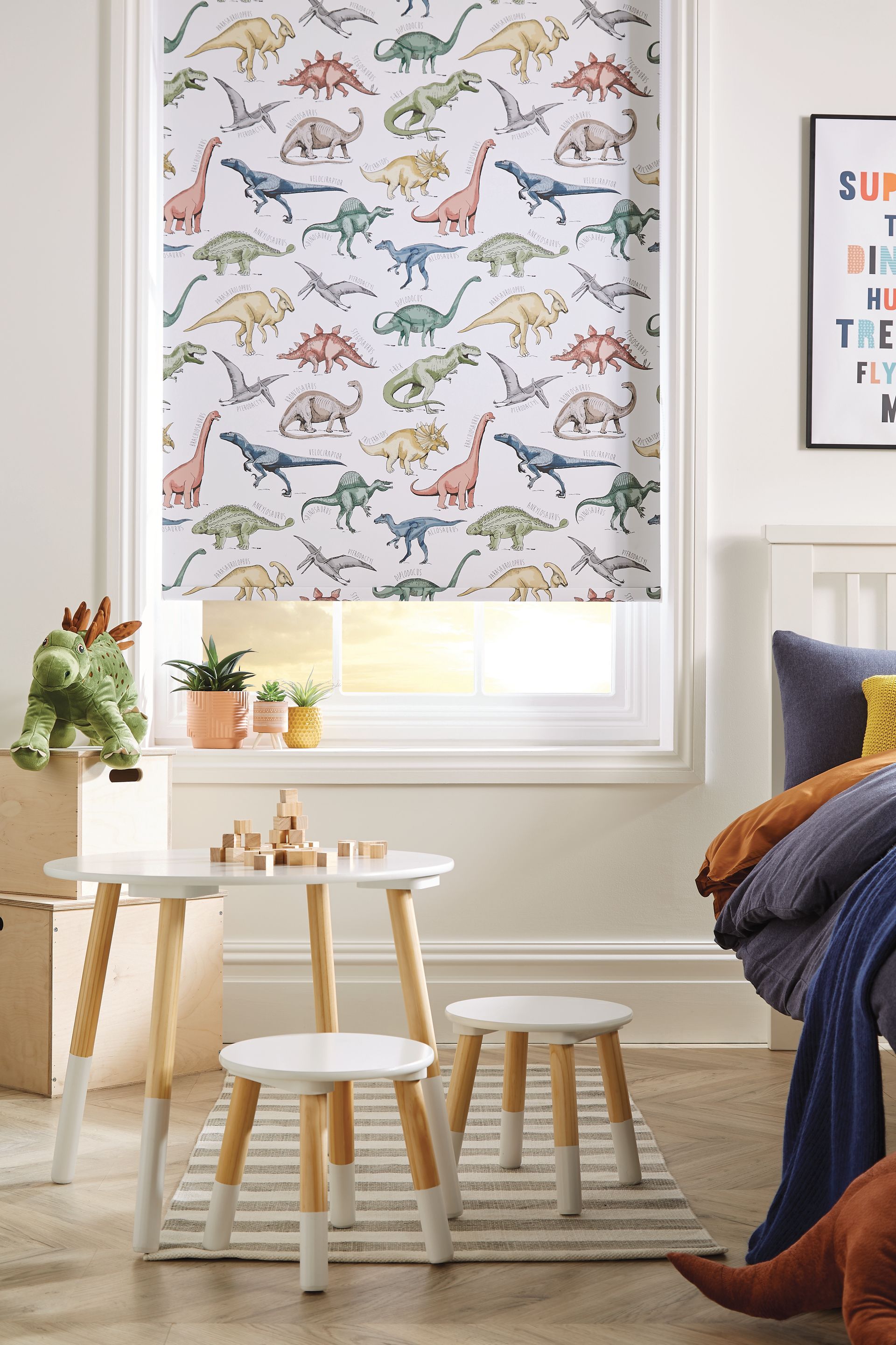 A bedroom with a bed , table and stools and a window with a dinosaur blind.