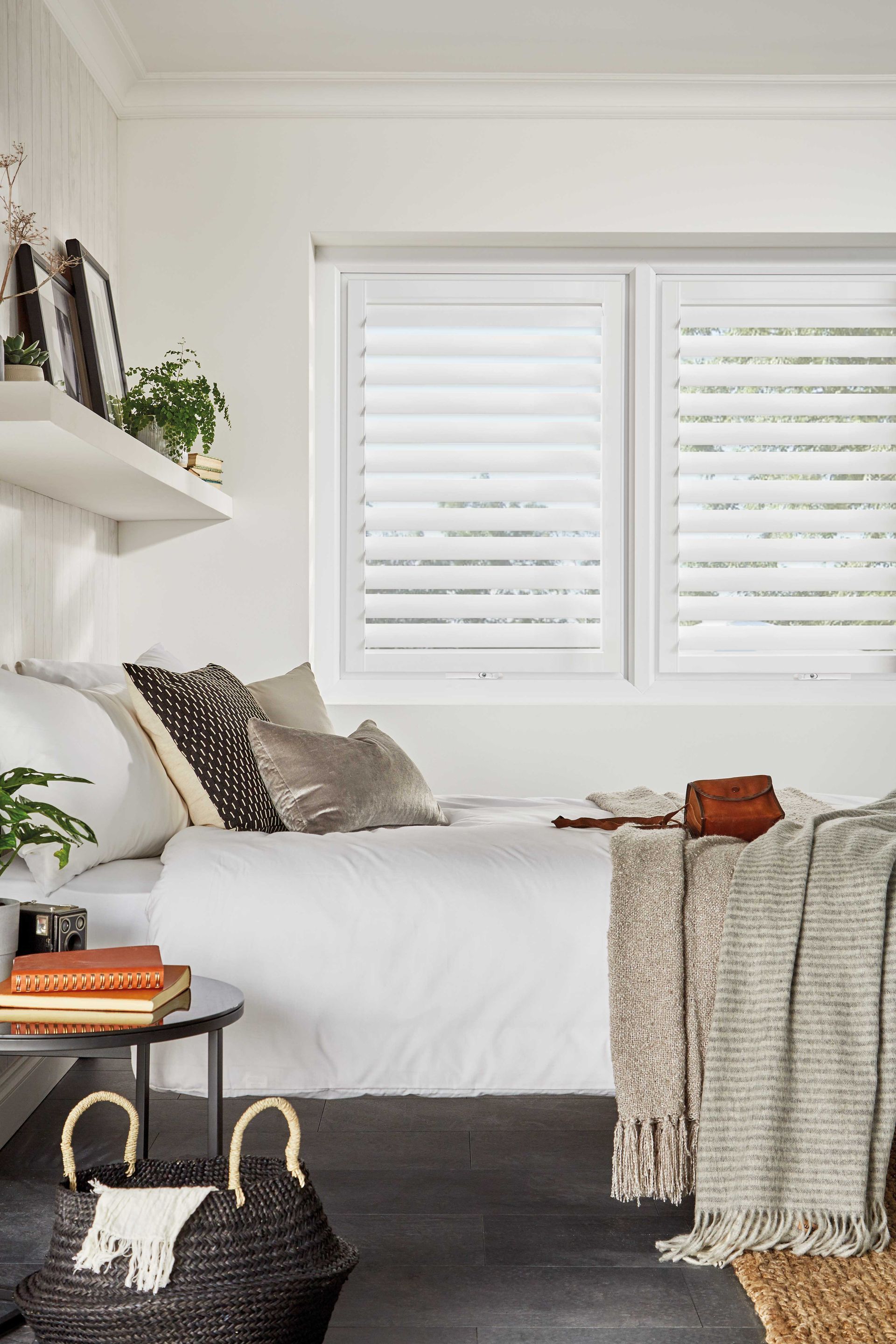 A bedroom with a bed , a table , and a window with white shutters.