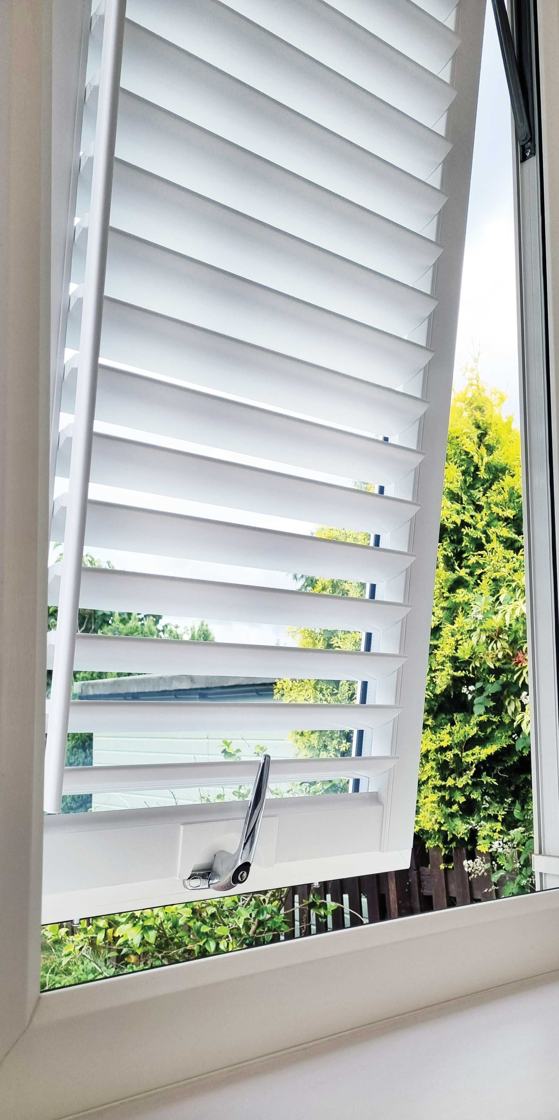 A close up of a window with white shutters on it.