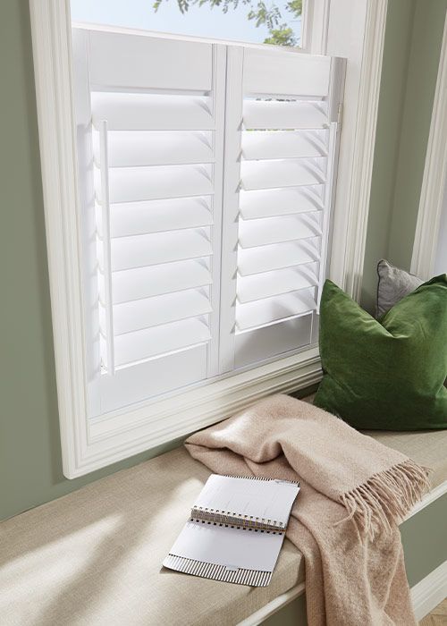 A window seat with white shutters and a green pillow.
