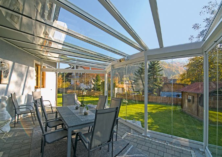 A patio with a table and chairs under a glass roof