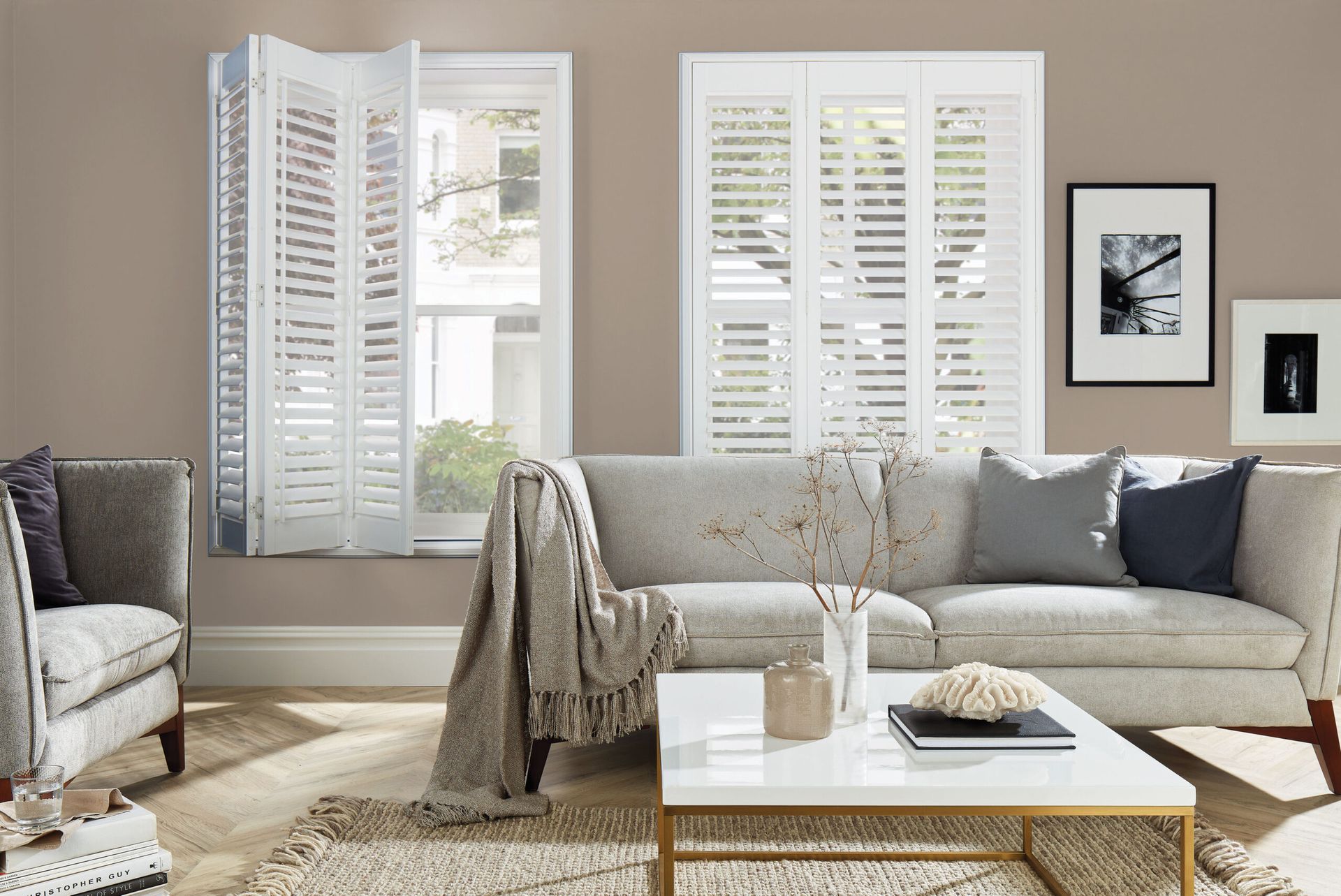 A living room with a couch , chair , coffee table and shutters on the windows.