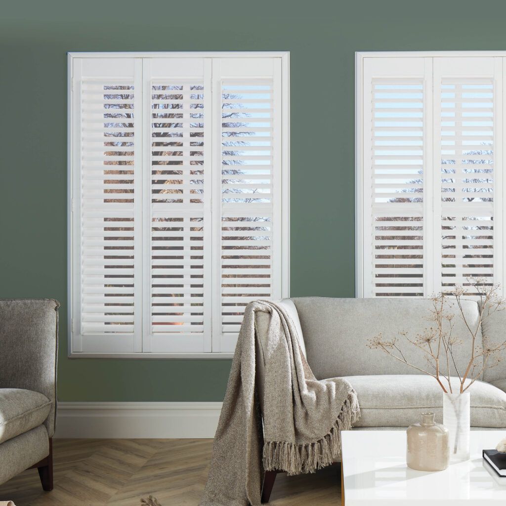 A living room with green walls and white shutters on the windows