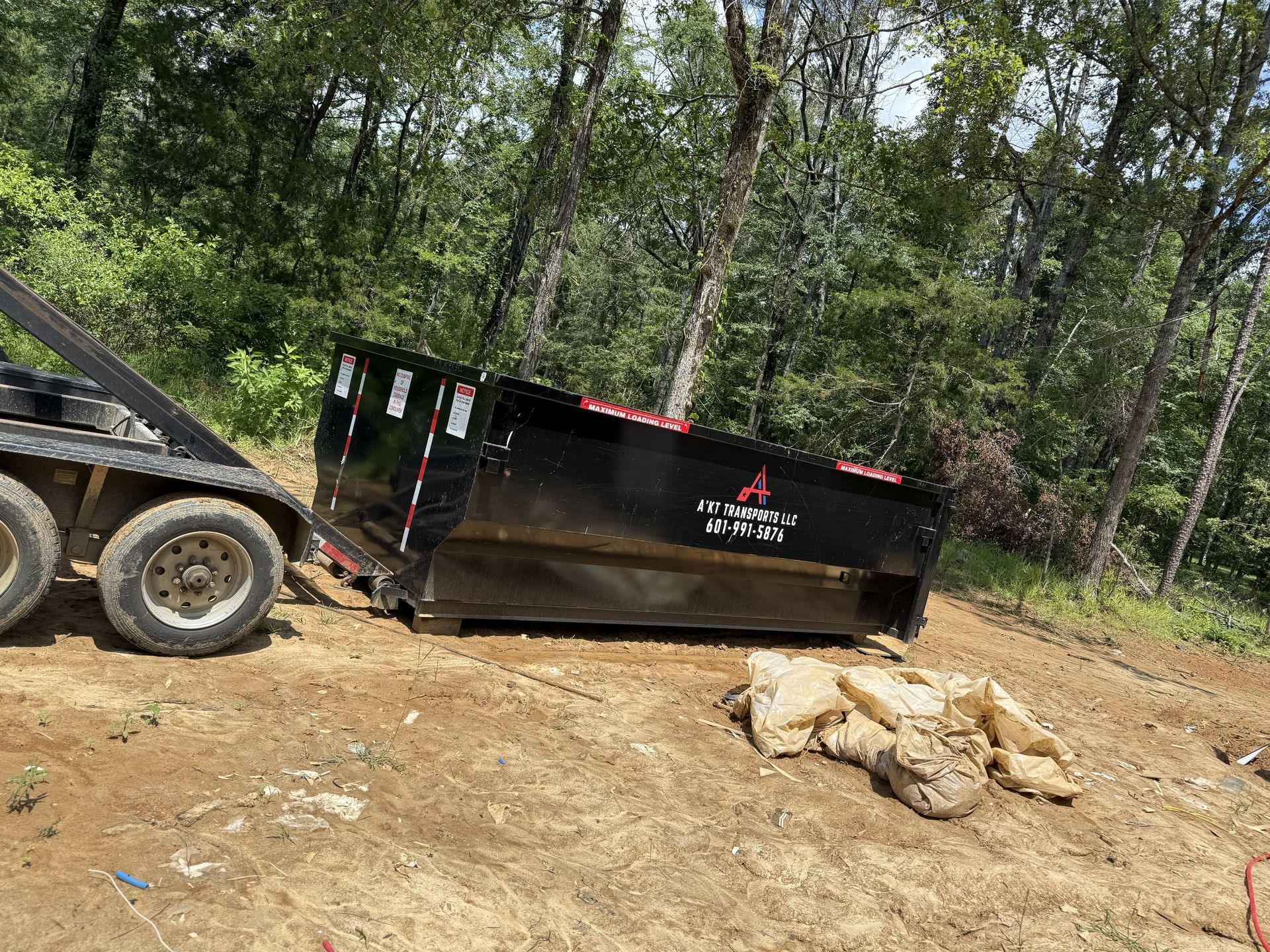 A dumpster is being pulled by a truck on a trailer.