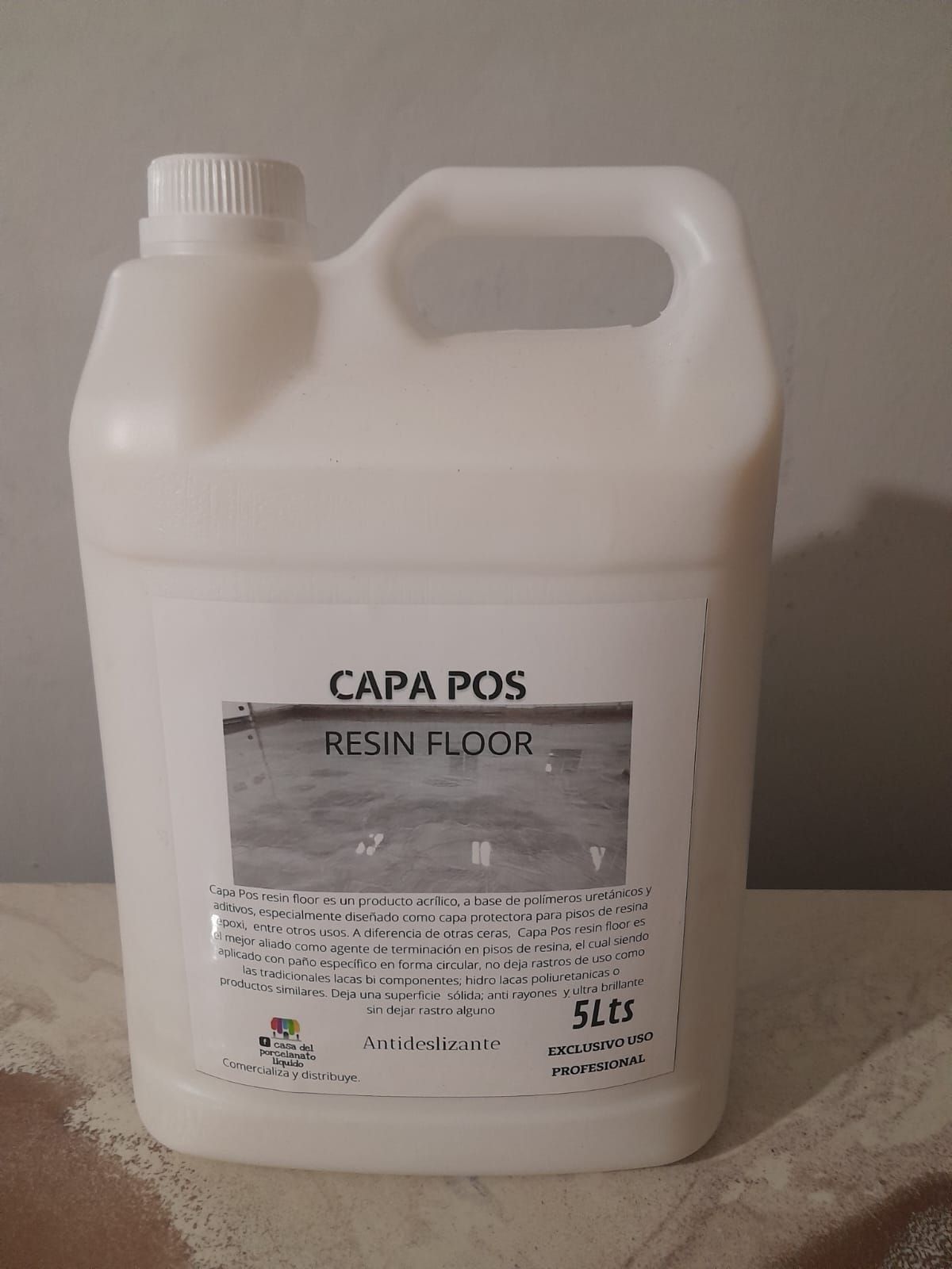 Contenedor blanco rotulado “CAPA POS RESIN FLOOR” con asa, sobre una superficie, sobre un fondo gris.