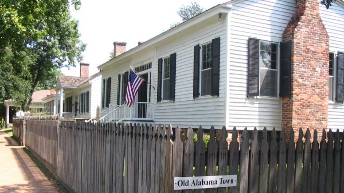 Lucas Tavern in Old Alabama Town, Montgomery, AL shown with black shutters behind a wooden fence.