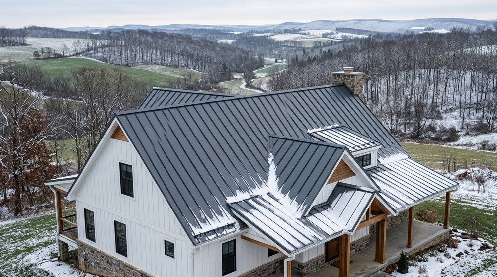 Charcoal standing seam metal roof on a Pennsylvania farmhouse, shedding snow in winter .