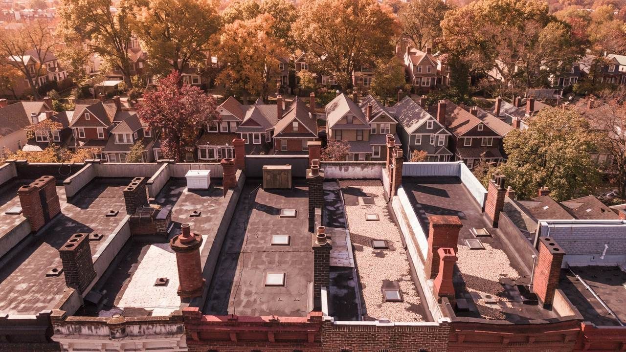 Aerial view of brick row homes with flat rear roof sections and parapets in Reading, with gabled houses beyond