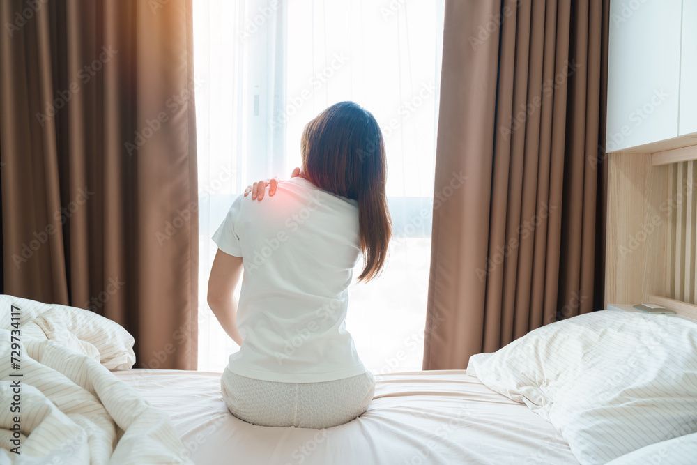 Person sitting on a bed in a bright room, looking out a window with curtains.