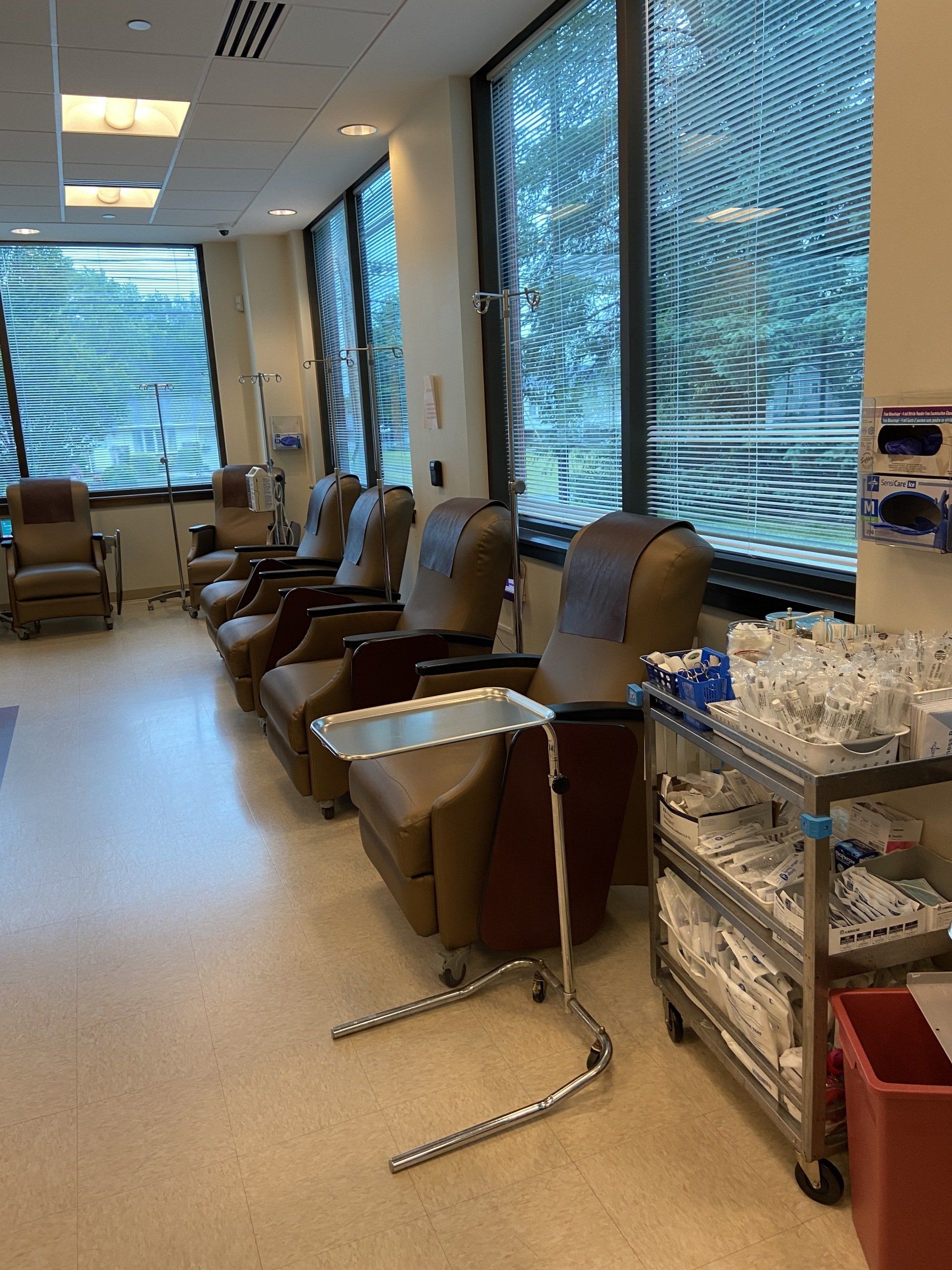 Chemotherapy treatment room with recliner chairs, windows with blinds, and medical supplies.