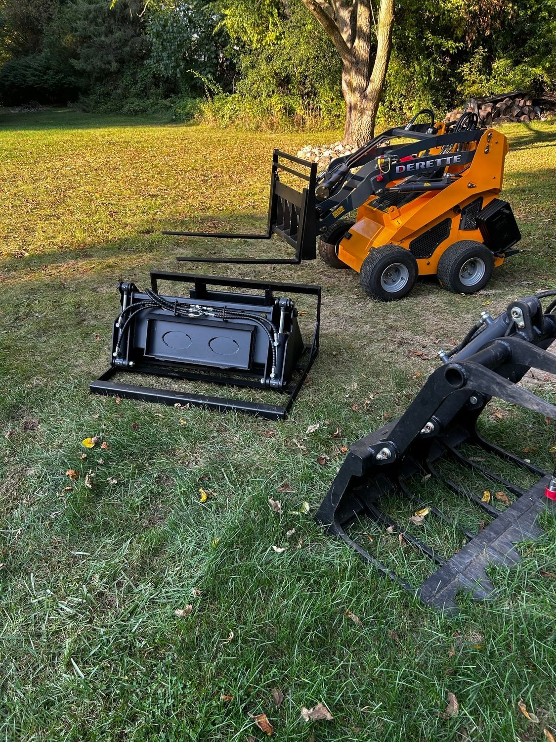Orange skid steer and detached mower attachment on a grassy lawn near a tree.