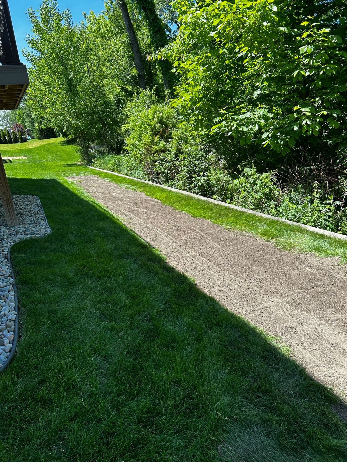 Gravel path through a sunny green garden beside a stone building and dense trees