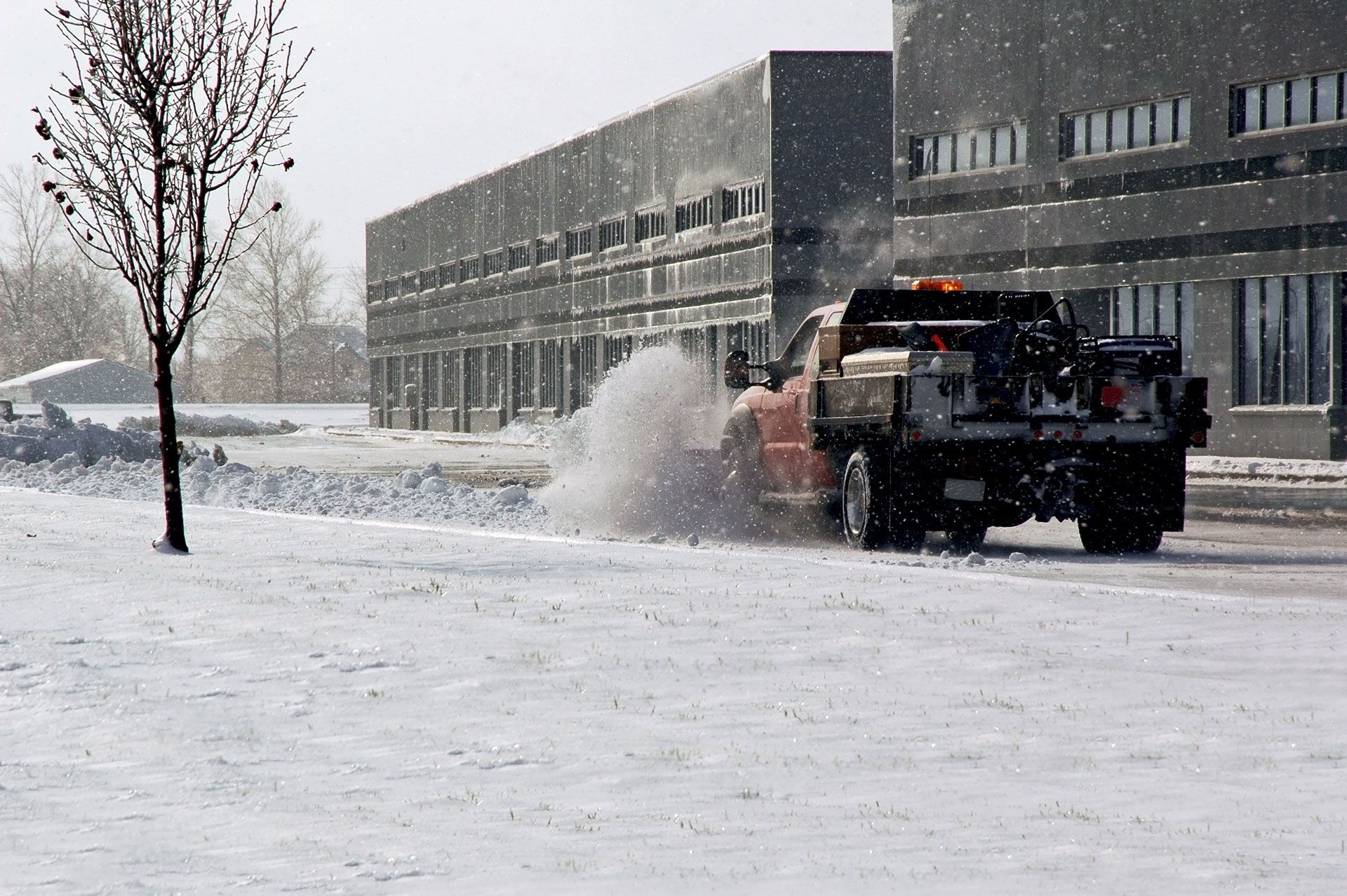 Truck plowing snow beside a building in a snowy winter scene
