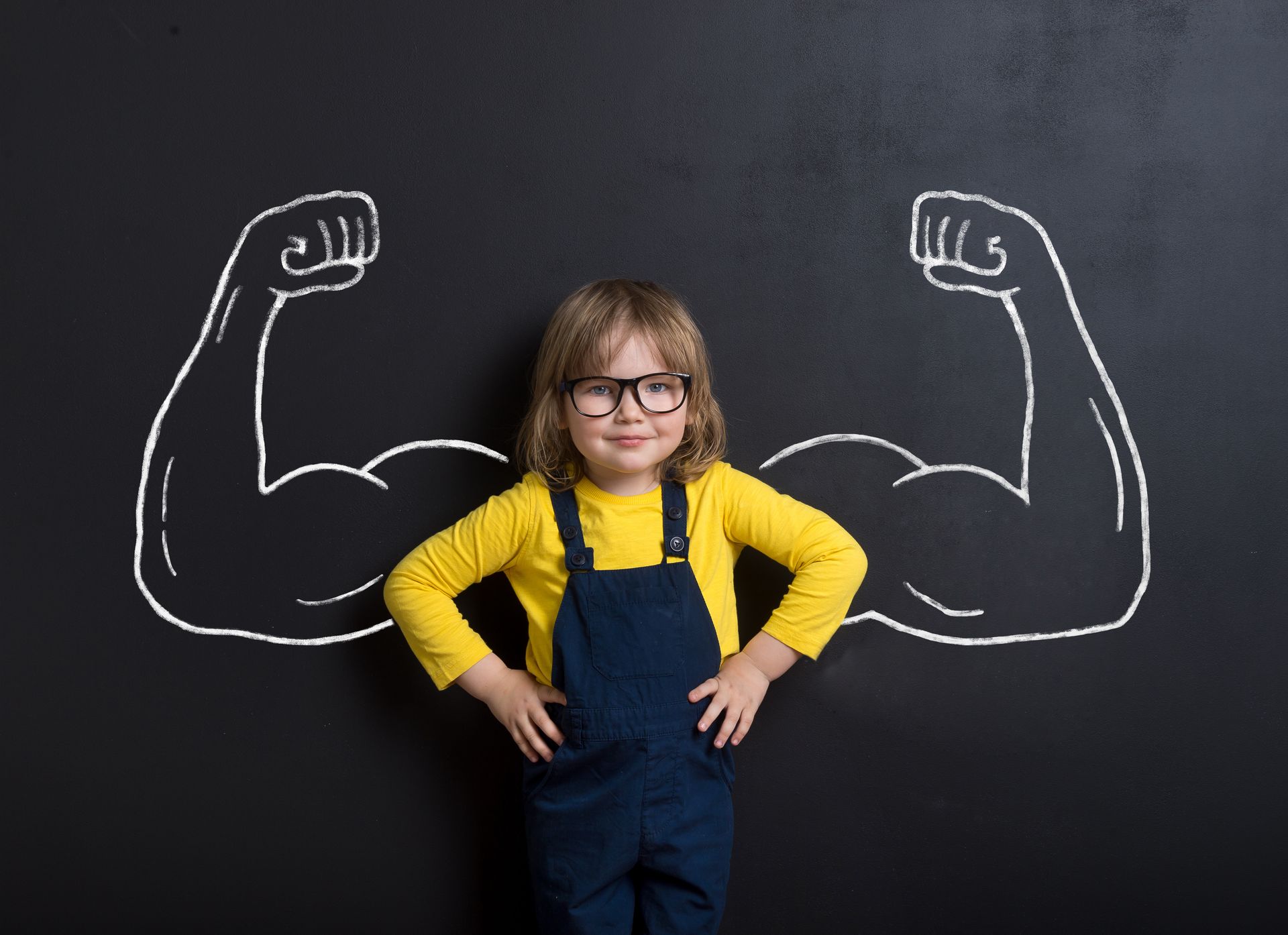 a little girl is standing in front of a blackboard with muscles drawn on it .