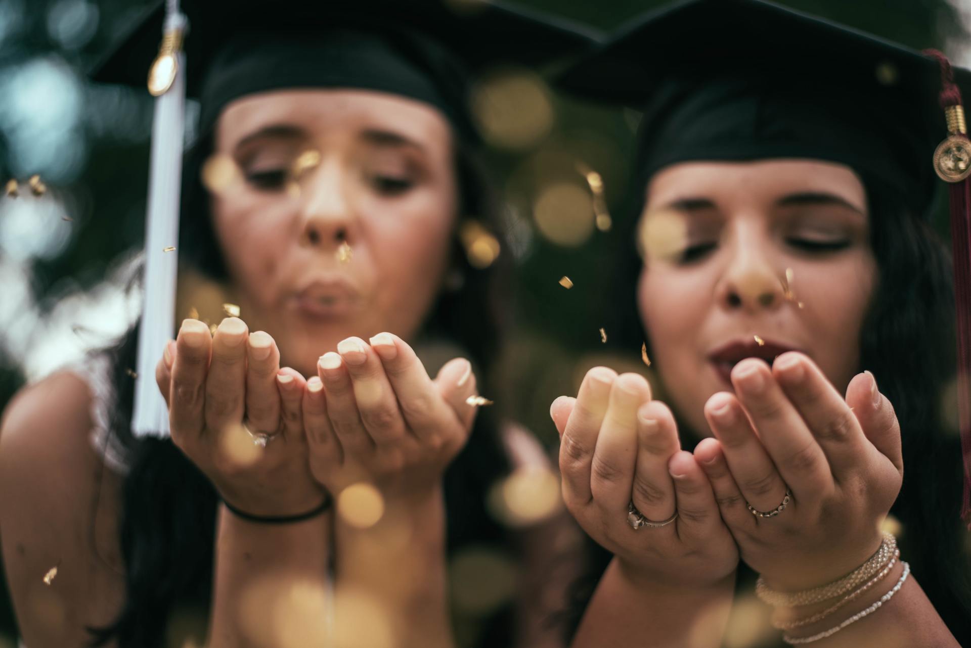 Two female graduates are blowing confetti into the air.