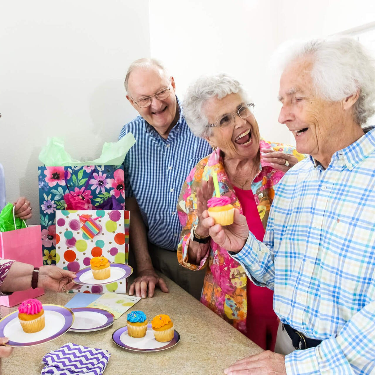 Group of retired friends celebrating with colorful cupcakes and presents Vibrant group of retirees celebrating a man's birthday