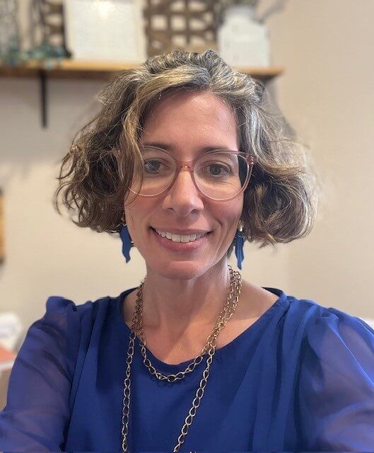 A white woman with medium brown and gray hair and glasses in an office