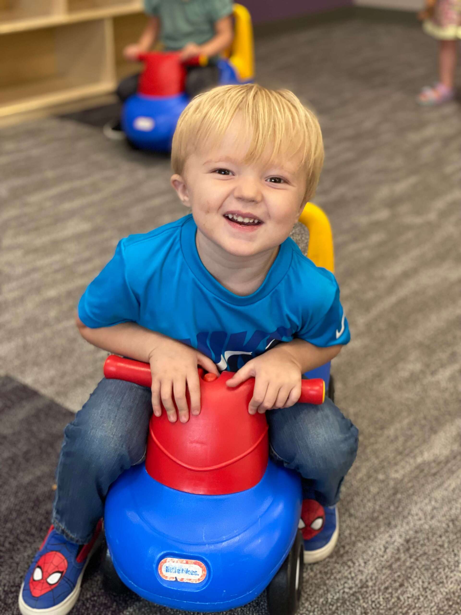Child riding a toy car at It Takes a Village Childcare