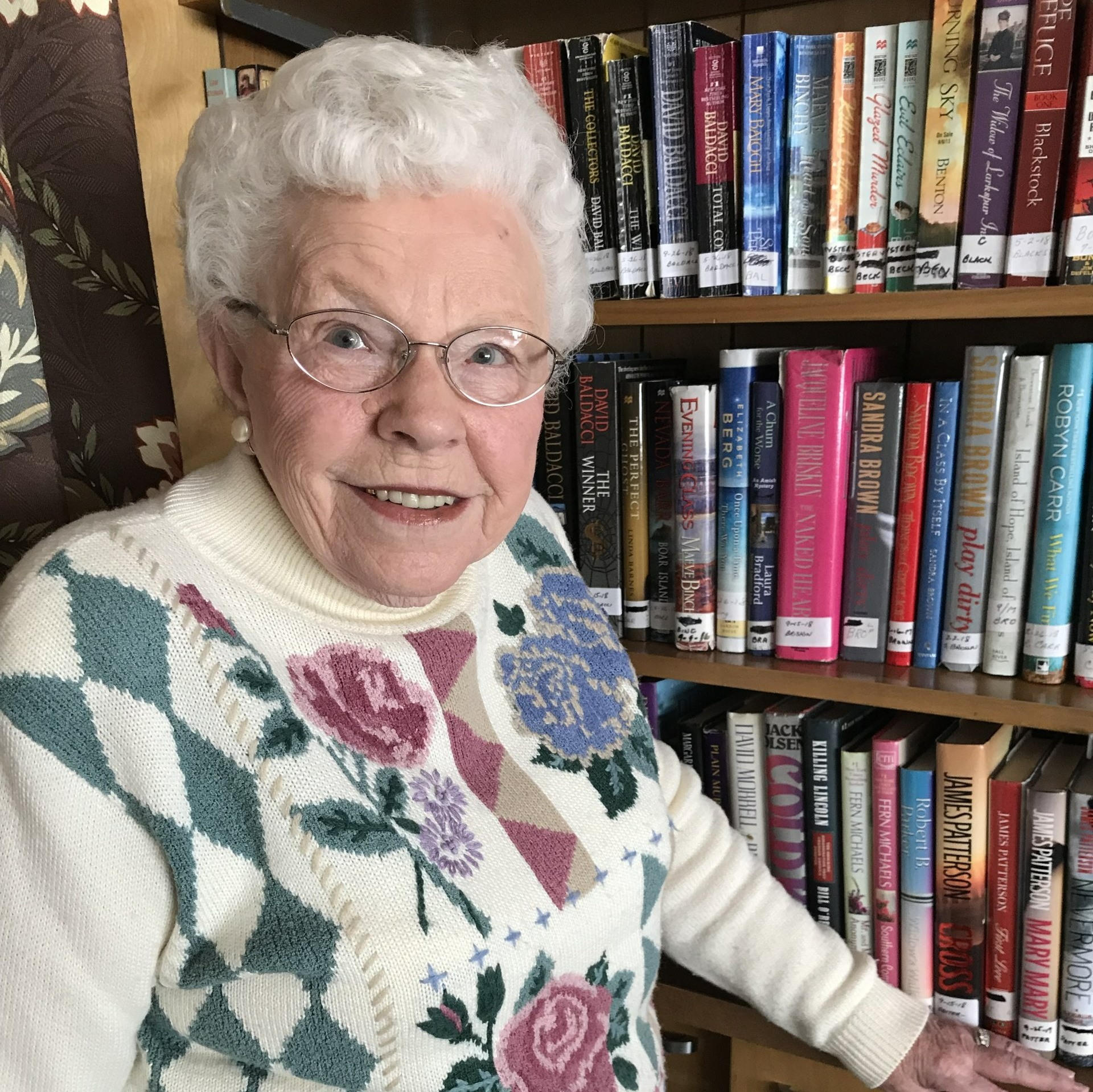 senior lady standing in front of a book shelf full of books senior lady standing in front of a book shelf full of books
