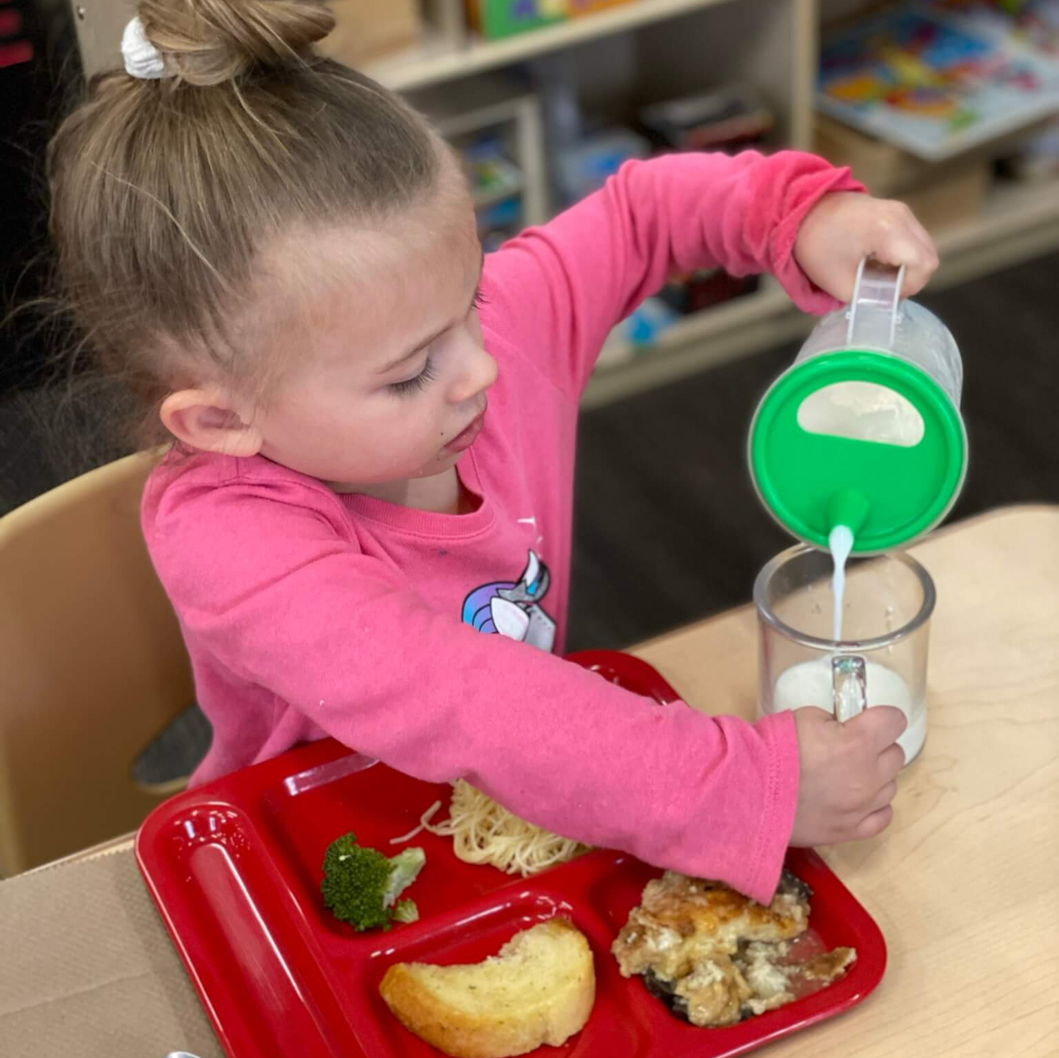 Young girl pouring milk into a cup with her meal in front of her
