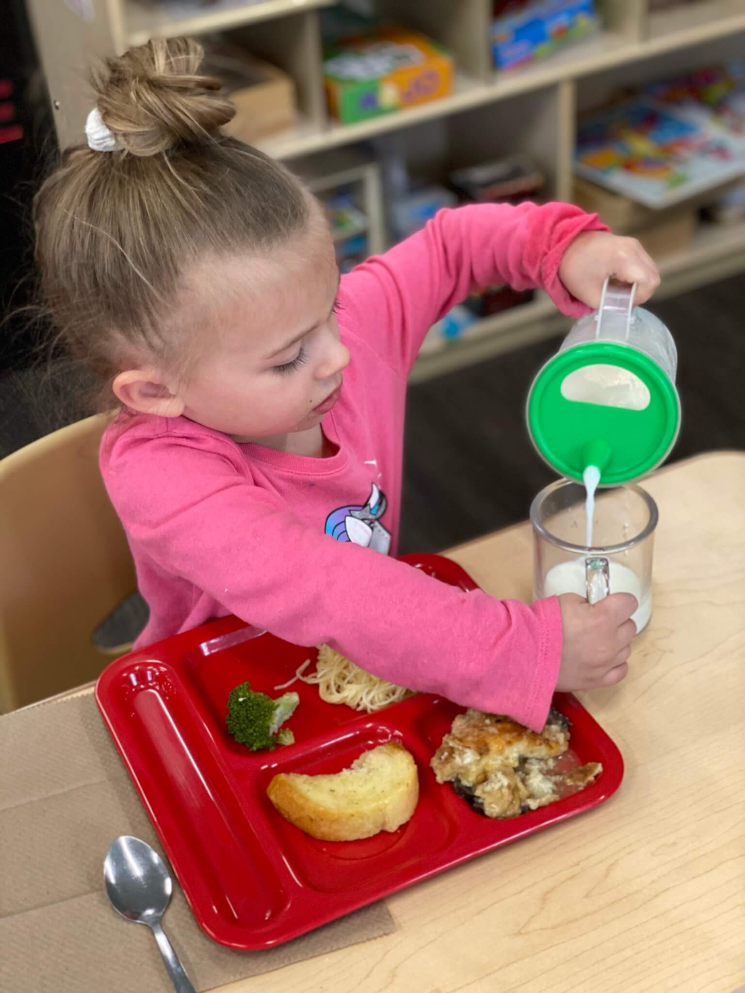 Young girl pouring milk into a cup with her meal in front of her