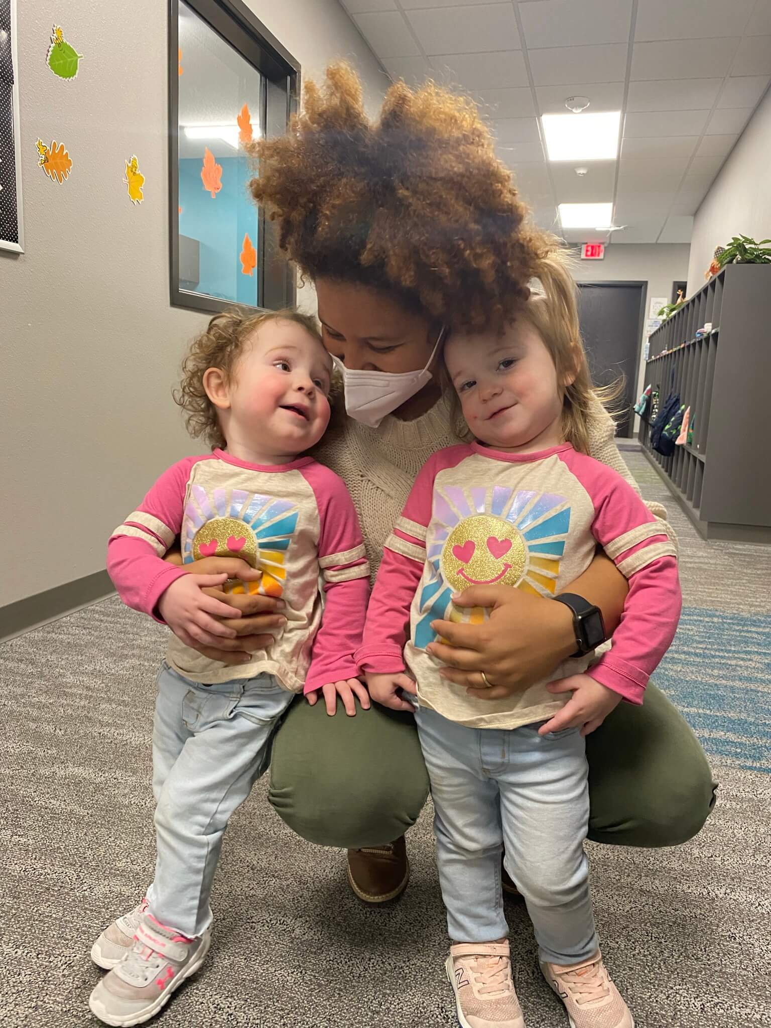 It Takes a Village Childcare employee bent down hugging twin girls