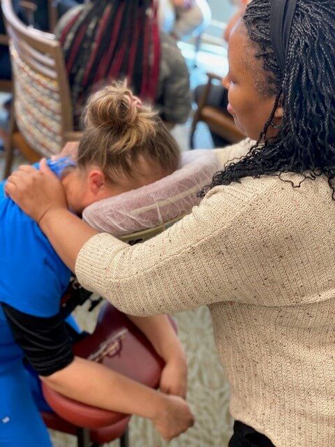 licensed massage therapist giving a massaging the shoulders of employee sitting in a professional massage chair