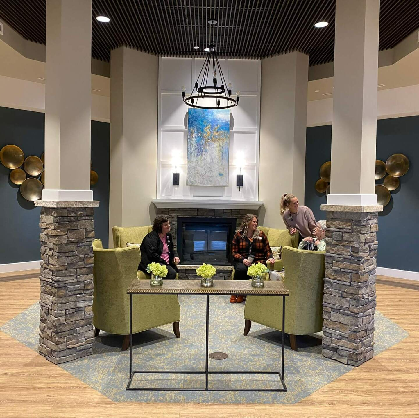 resident and employees gathering near the fireplace located in the entry way of Wellspring Living Health Center
