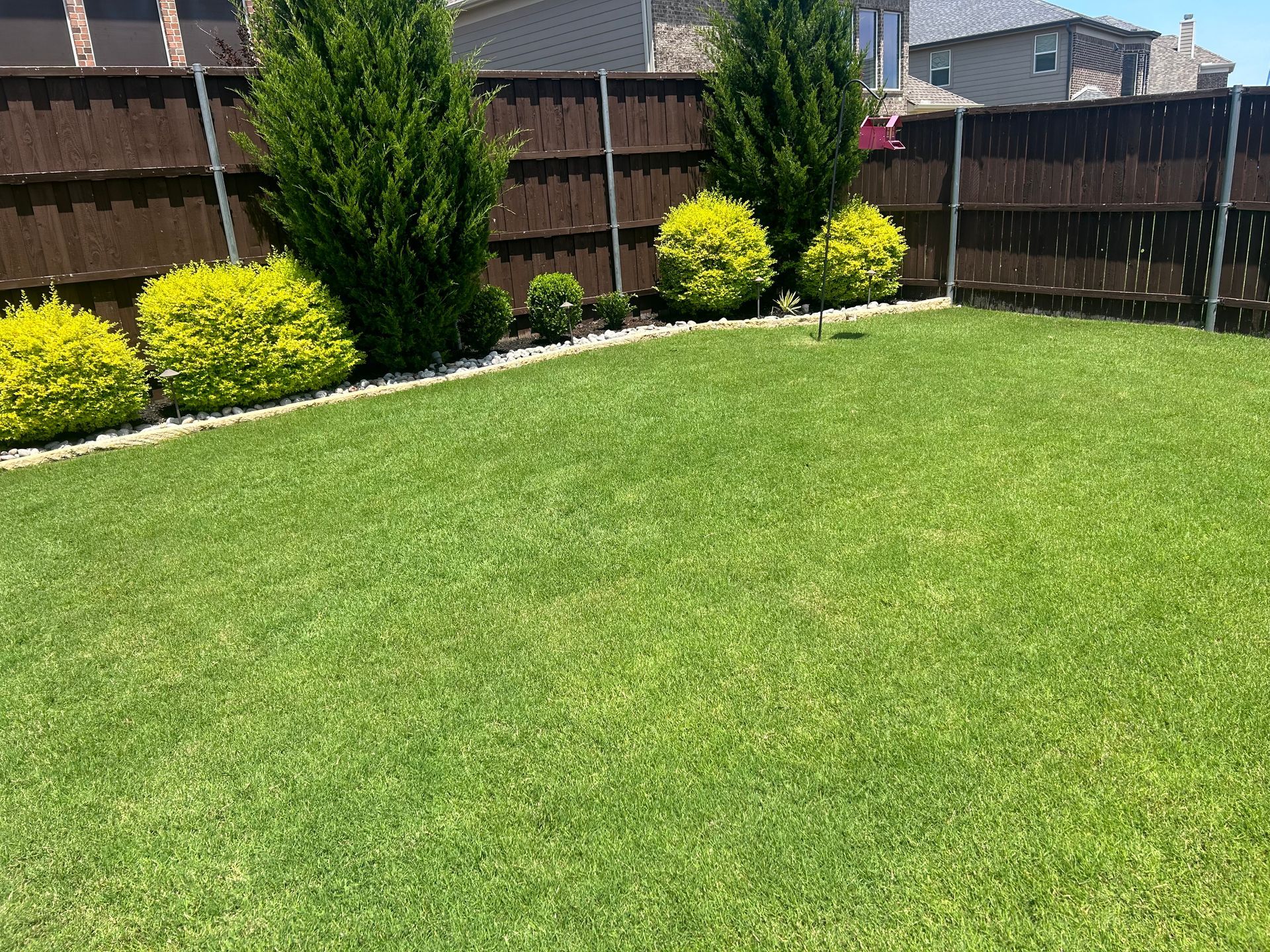 A backyard with a fence and a lush green lawn