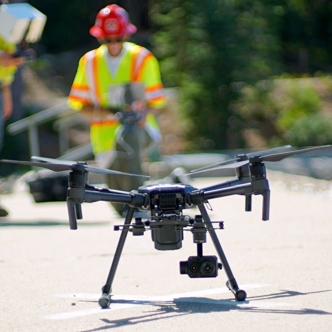 Drone inspecting a road, with a worker in a safety vest blurred in the background