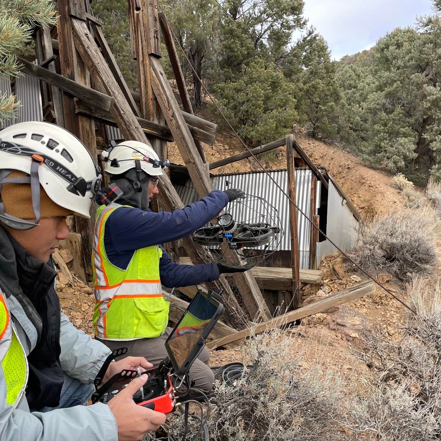 Two helmeted workers in safety vests monitoring equipment near a damaged hillside structure