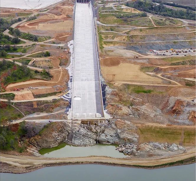 Aerial view of a concrete dam spanning a rocky valley with water below and construction site around it